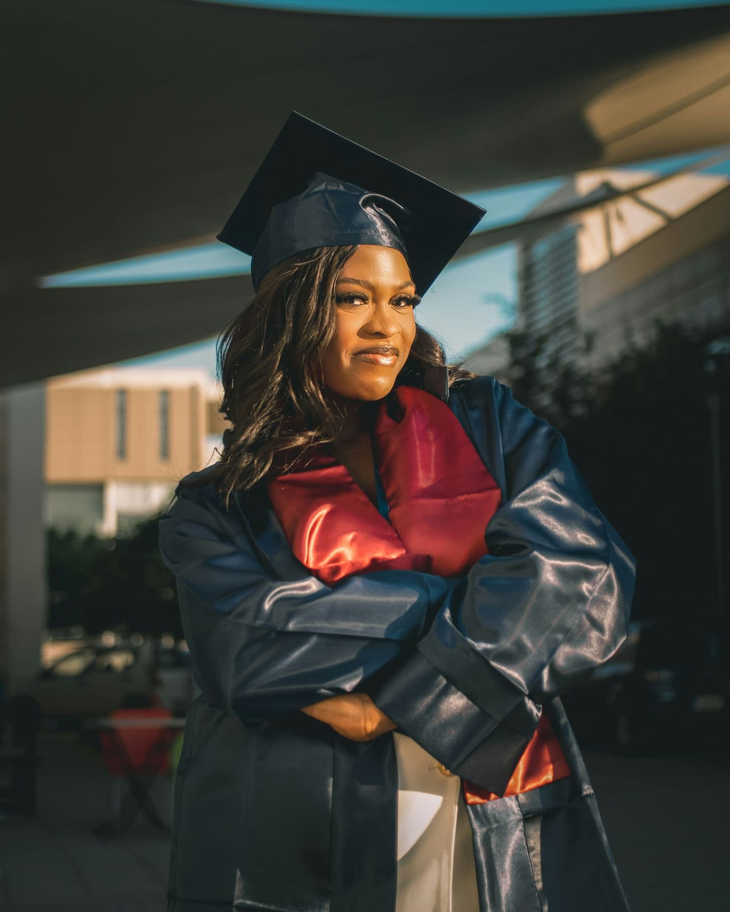 A graduate in cap and gown, arms folded, smiling